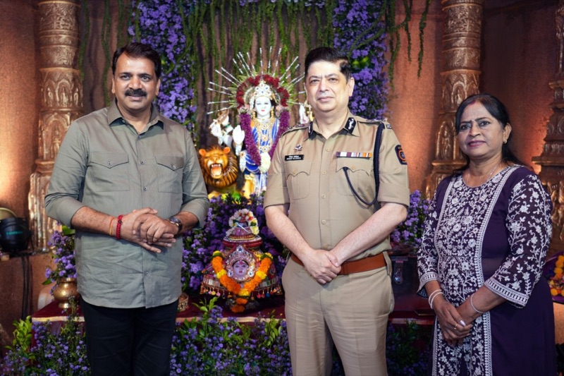 Niket Kaushik, IPS, in uniform at a community festival pandal, standing with two residents in front of a decorated shrine.