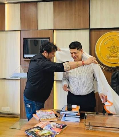 Niket Kaushik being welcomed with a ceremonial shawl by a visitor at his office.