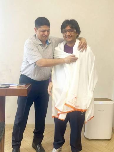 Niket Kaushik placing a ceremonial shawl around a guest during a meeting.