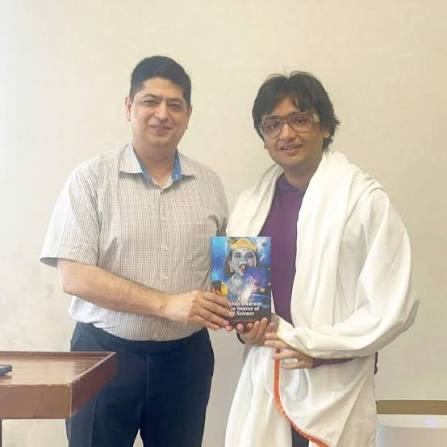 Niket Kaushik being presented with a book by a visitor during a meeting.